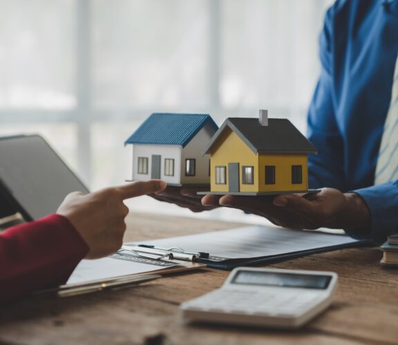 A person holding two home models in their hands and another person pointing