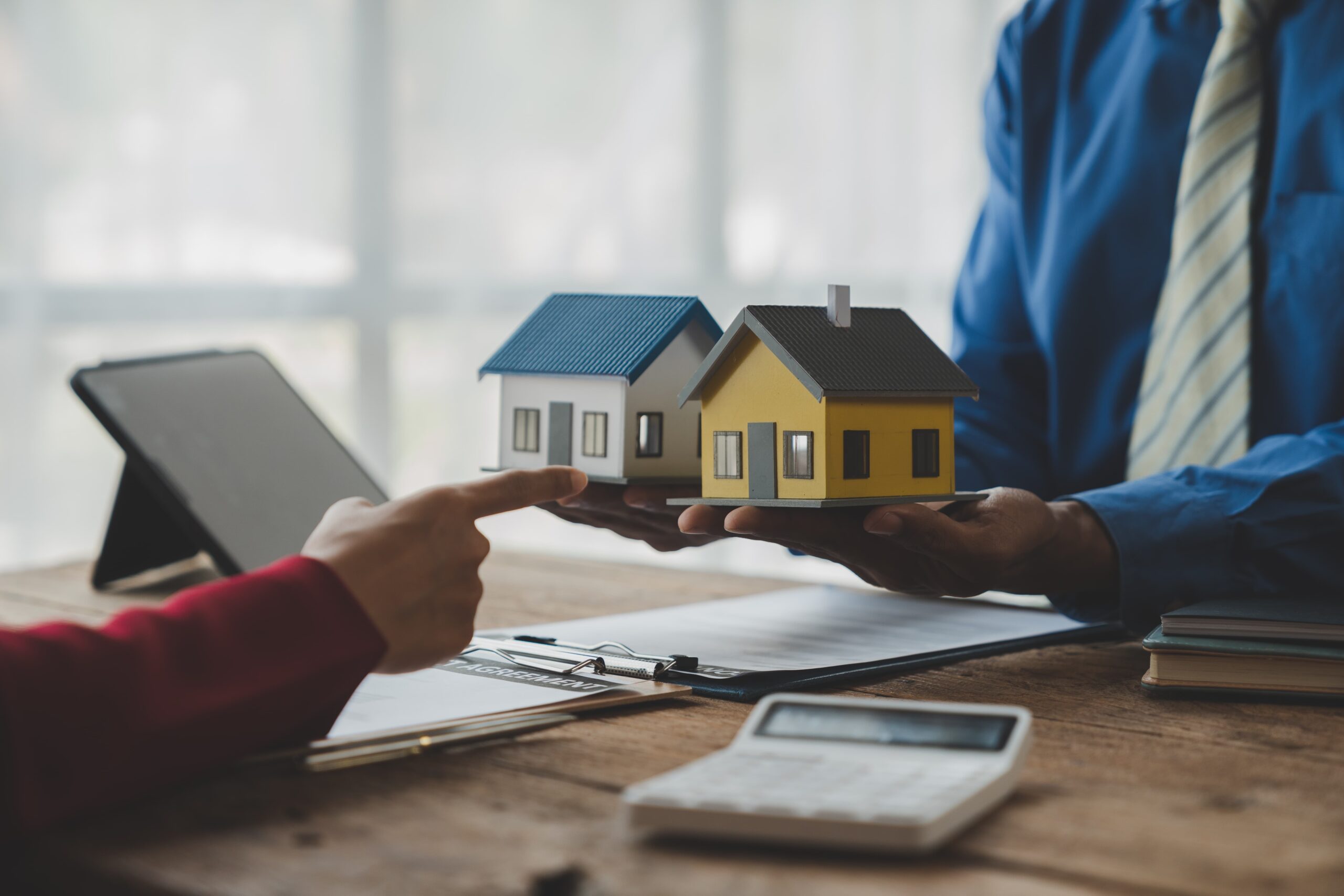 A person holding two home models in their hands and another person pointing